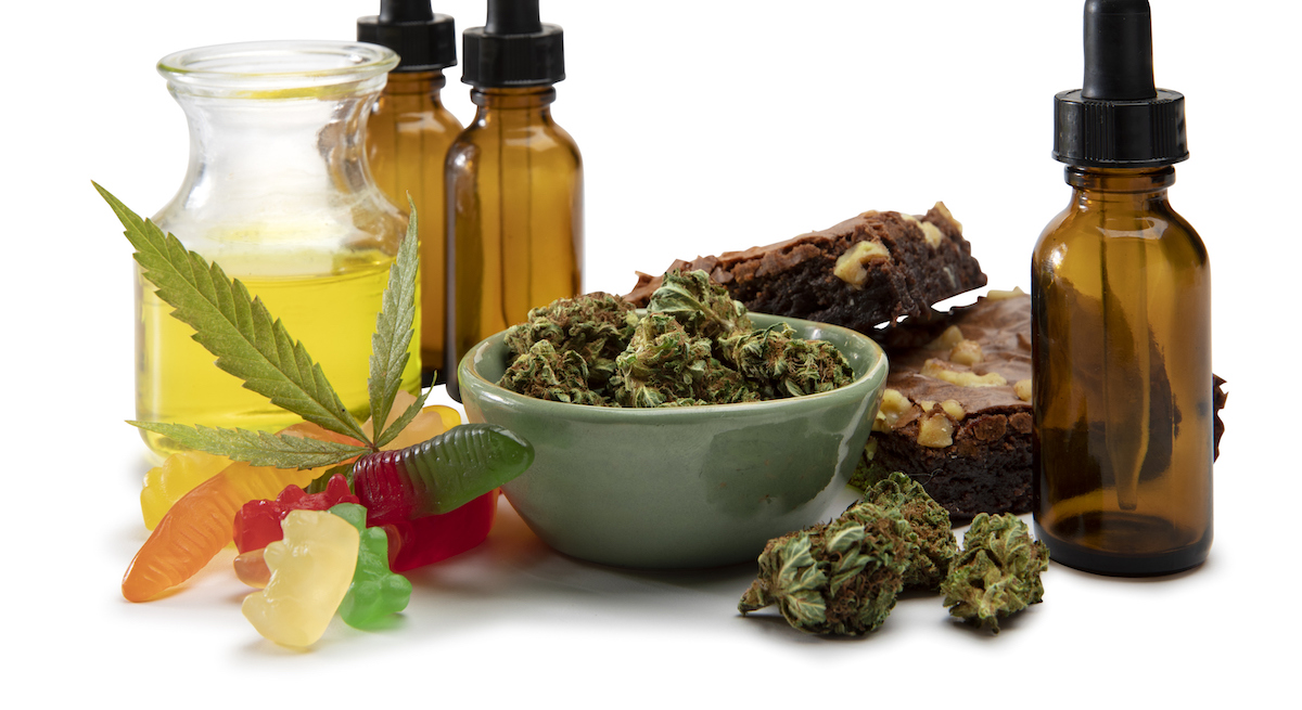 Cannabis oils and bud in a small bowl surrounded by sweet edibles