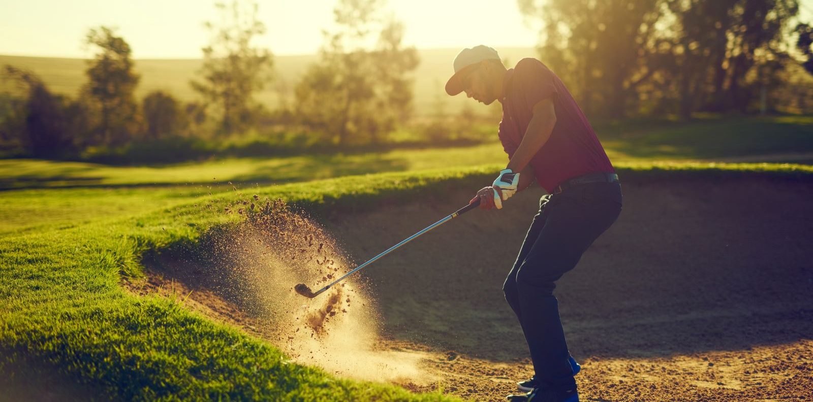 Man swings at a golf ball in sand.